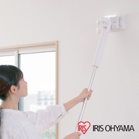 一位女性正使用白色機身、銀色金屬握桿的電動平板拖把清潔牆面。拖把頭為透明方形，裝有白色清潔墊，並有LED燈照明。