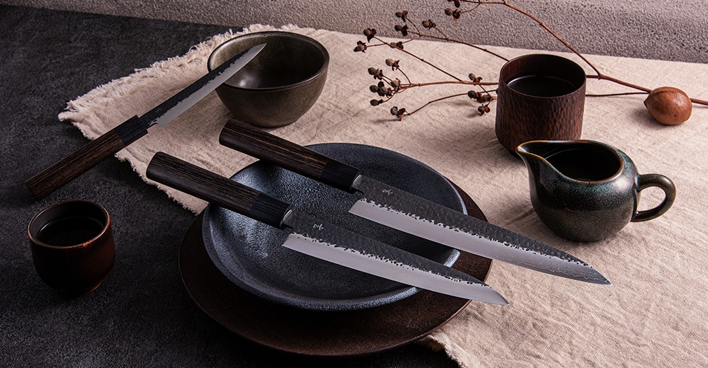 玄 / Petit knife 水果刀，刀刃為銀色不銹鋼材質，帶有錘紋和黑色漸層，刀柄為深棕色木質。另有黑色陶碗、深棕色木杯、綠色漸層陶瓷小壺及裝飾樹枝。