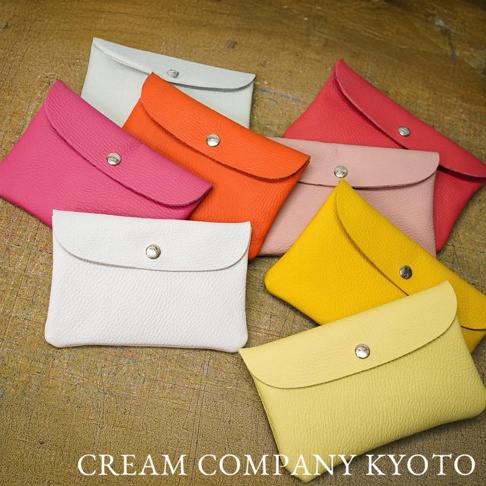 多個由皮革製成、顏色各異（包括白色、淺灰、粉紅、桃紅、橙色、黃色、淺黃色）的京都職人手作多功能收納包，皆有按扣封口設計，以俯視角度陳列。