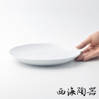一個白色的波佐見燒 Common 陶瓷料理盤，直徑 24 公分，盤面平坦，邊緣略微向上彎曲。一隻手輕輕握住盤子的邊緣。