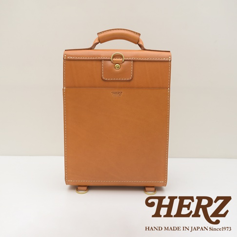 職人手作皮革復古後背包，採用棕色天然皮革，帶有金屬扣環和提把，包身線條簡潔，底部有四個金屬腳釘，整體呈現經典復古風格。