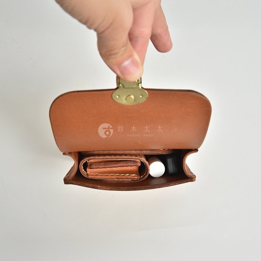 棕色皮革腰包，內部裝有卡夾、口紅和其他小物，採用復古金屬開關，由手持開啟，展現職人手作質感。