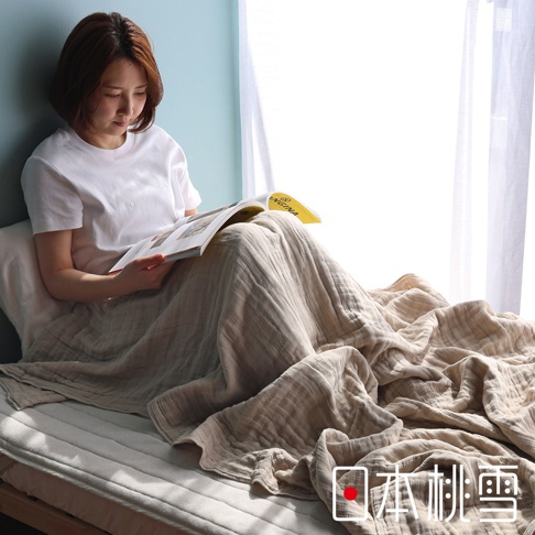 一位女子坐在床邊，蓋著一件米色五層紗被，正在閱讀一本雜誌，雜誌的封面上有「VIRGINIA」字樣，圖片下方有「日本桃雪」的文字標誌。