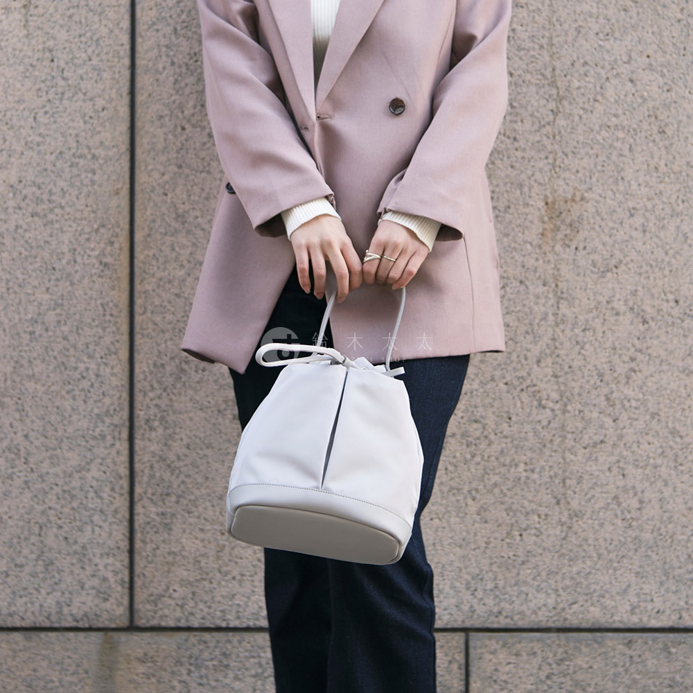 TUTUMU sacca Rich 抽繩水桶包，灰色柔軟材質，搭配淡粉色西裝外套，展現時尚都會風格
