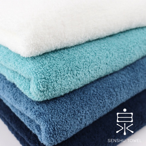 堆疊的浴巾，由上至下顏色由白、淺藍綠、藍綠、深藍構成，材質為柔軟長纖維。