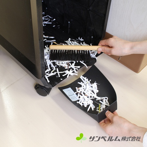 一雙手正在操作Sanbelm天然馬毛桌面掃把與畚箕組，將碎紙從黑色碎紙機底部清理至畚箕中，掃把刷毛細緻，整體呈現居家清潔與辦公環境整理的畫面。