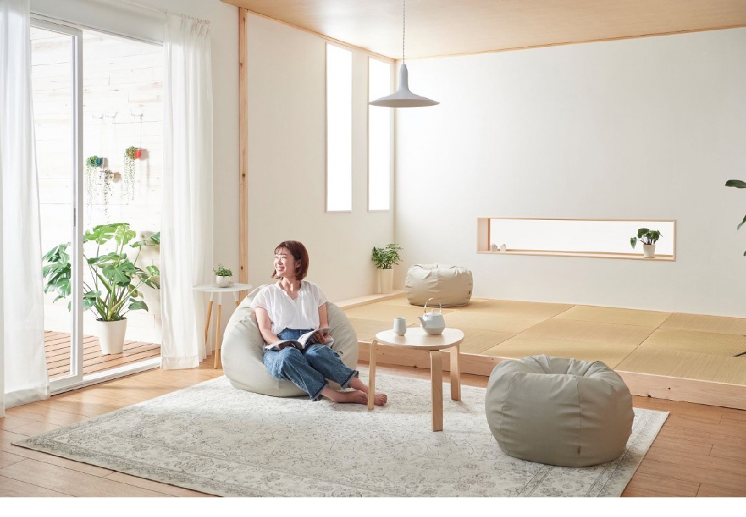 一位女性坐在淺米色皮革懶骨頭沙發上，手持一本書。房間內有另一張相同的沙發，以及一個淺木色圓形茶几。