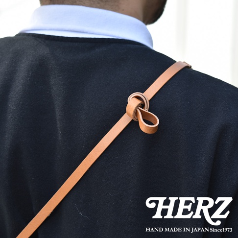 職人手作皮革直式隨身單肩包 CP-37，焦糖棕色皮革肩帶，以打結方式固定於黑色衣物上，展現簡約設計。