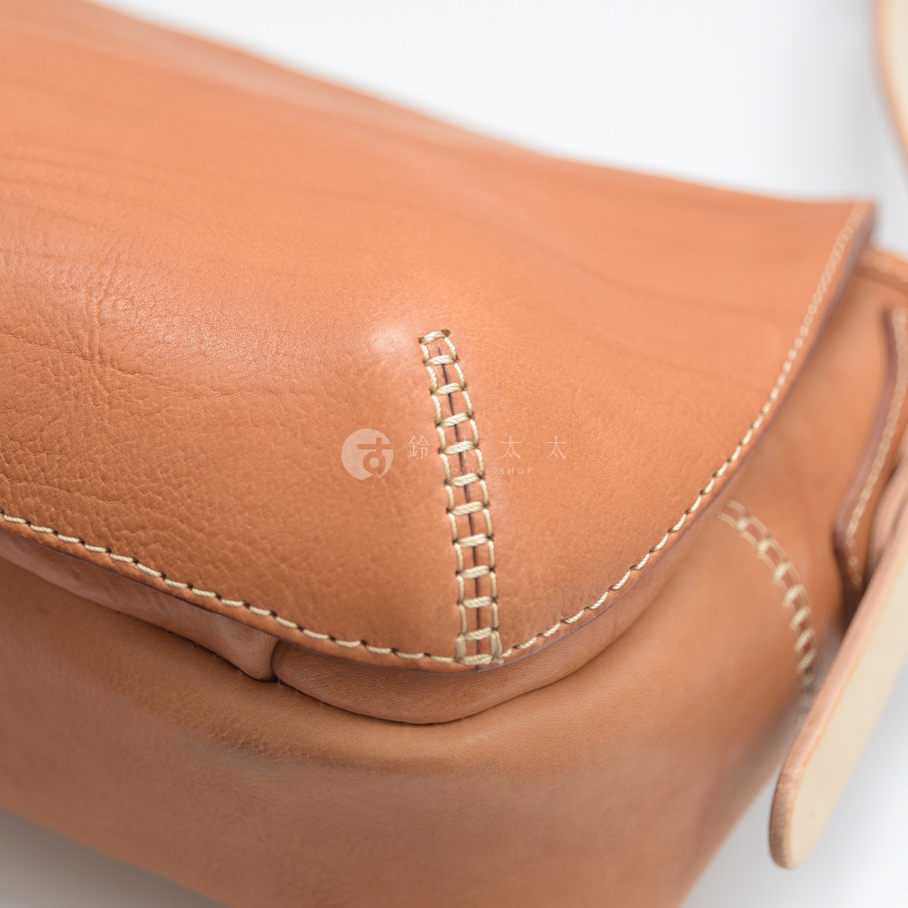 職人手作皮革郵差包，呈現溫潤的淺棕色調，材質為柔軟的皮革。包款帶有手工縫線點綴，展現細緻質感。