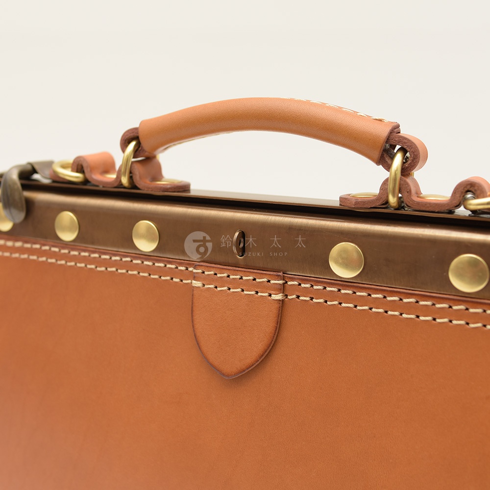 職人手作皮革復古口金兩用手提包，特寫展示包款的提把、金屬鎖扣、銅質鉚釘及縫線細節，皮革呈現溫潤的棕褐色。