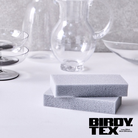 兩個淺灰色海綿刷疊放在白色表面上，背景為透明玻璃製品。