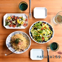 白色八角形餐盤盛裝義大利麵，盤邊有藍色線條圖案。旁邊的圓形藍紋餐盤盛有沙拉，內含萵苣、番茄、黃椒和起司。另有長方形白色餐盤盛裝章魚、番茄、黃瓜與洋蔥沙拉。畫面中有綠色玻璃杯、銀色叉子與夾子。