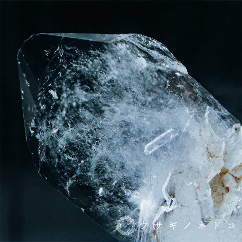 透明無色水晶礦石，內部可見細小晶體與紋理，晶體表面光滑，部分區域略帶雜質，背景為深色。