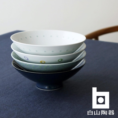 堆疊的四個陶瓷茶碗，由上而下分別為：白色帶淺綠色圓點、白色帶彩色圓圈（紫、黃、綠）、淺藍綠色帶彩色圓圈、深藍色。