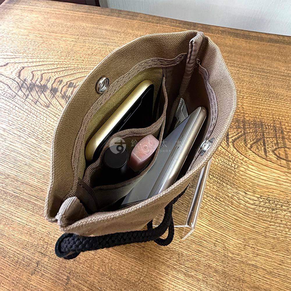 帆布手機包內裝有手機、口紅和另一個銀色物品，包包的背景是木桌。