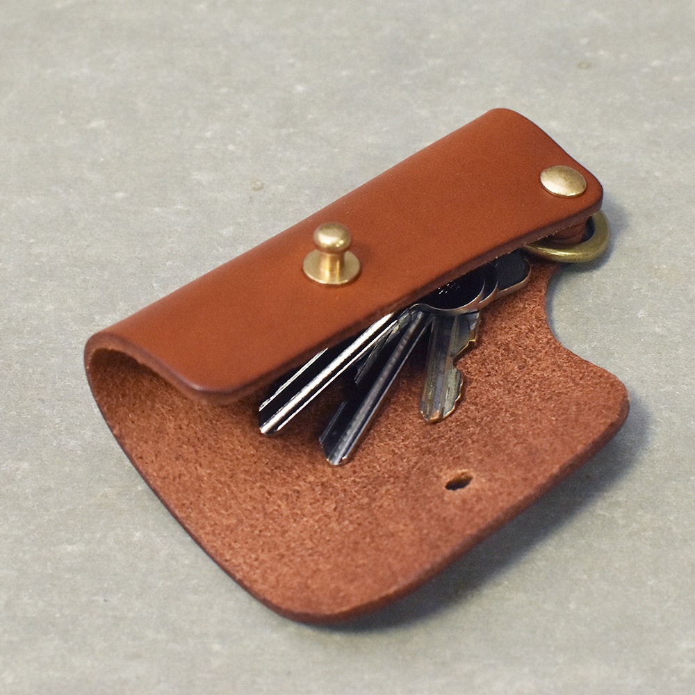 職人手作咖啡色皮革鑰匙套，內含多把金屬鑰匙，以黃銅壓扣固定，另有黃銅掛環。