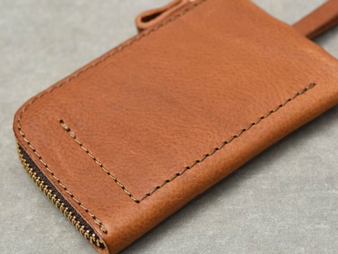 職人手作咖啡色皮革鑰匙包，有拉鍊開合，縫線精緻，頂部有皮革掛繩。