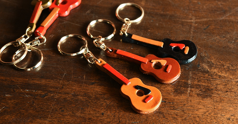 職人手作皮革吉他造型鑰匙圈，共有棕色、黑色等款式，附有銀色金屬鑰匙圈。