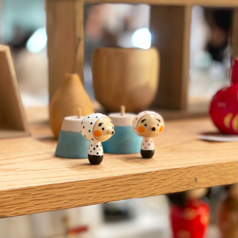 木製擺飾，兩個卡通風格的小人偶，頭戴白色 polka dot 頭巾，身穿黑色或紅色 polka dot 上衣，臉部表情生動，周圍有藍色和白色錐形擺飾。