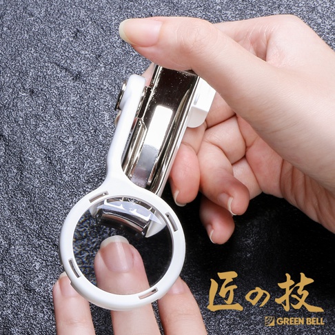 一只手持著白色外殼、不鏽鋼材質的指甲剪，放大鏡正對準指甲。