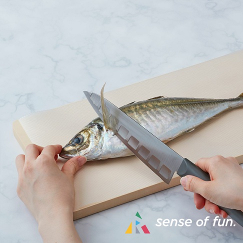 一條魚放在米色捲筒式砧板保潔墊片上，兩隻手正用一把刀處理魚。