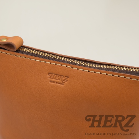 職人手作皮革三角收納包 KF-1，展示棕褐色皮革材質，帶有金色拉鍊和標誌性燙金壓紋。