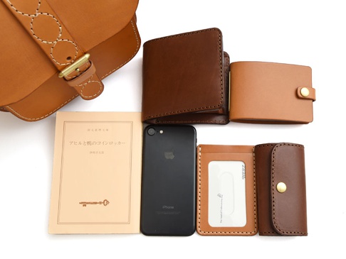 職人手作皮革十字繡紋單肩包，搭配棕色皮革短夾、淺棕色皮革對折夾、黑色手機、卡夾與鑰匙包，皆以精緻車縫線工藝呈現。