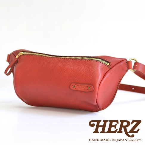 紅色職人手作皮革輕便斜背包，設有金色拉鍊及品牌標誌。