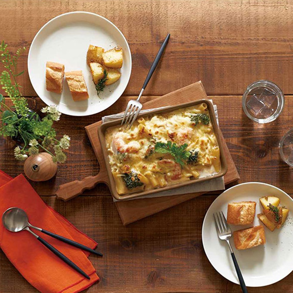 美濃燒釉彩萬用長方烤盤，裝有焗烤義大利麵，盤身呈棕褐色，附有木質烤網架，旁邊擺放著法國麵包、烤馬鈴薯和餐具。