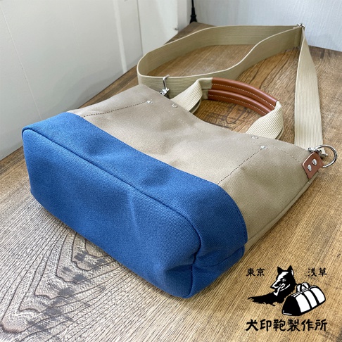 犬印純棉帆布兩用雙色托特包，主體為米白色帆布，底部與側面有一條藍色寬條紋，搭配皮革提把與米色織帶肩帶。