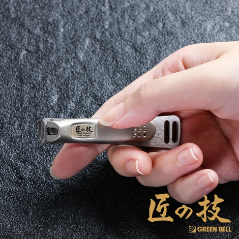 一只手正握著一支銀色不鏽鋼曲刃指甲剪，指甲剪上有日文「匠の技」及英文「High Quality Nail clipper」字樣。