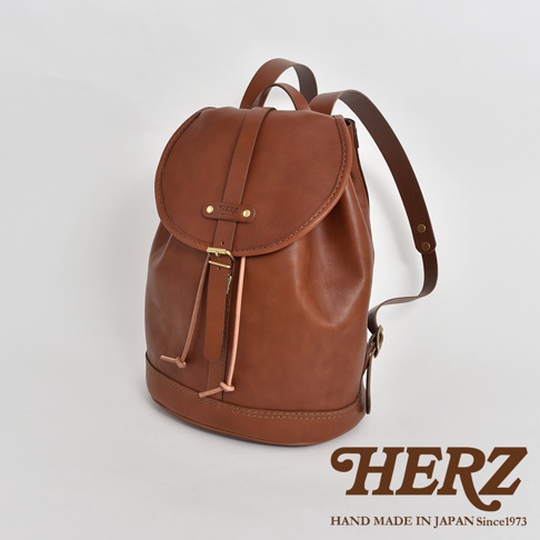 職人手作皮革單扣束口後背包，採用棕色牛皮製作，設有單一主隔層，束繩開口，外觀簡潔，配有可調節肩帶。