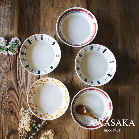 五個白色陶瓷盤，盤緣飾有格紋圖案，包含紅色、藍色、黑色和棕色線條，其中一個盤子內放有木製湯匙。