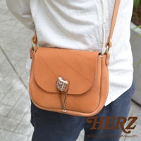 棕色皮革製成、帶有鹿角扣與細繩的圓弧形翻蓋肩背包，皮革表面有壓紋。