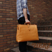 職人手作皮革軟式杜勒斯包，淺棕色皮革，方形包身，有頂部提把及金屬扣環，適合商務或旅行使用。