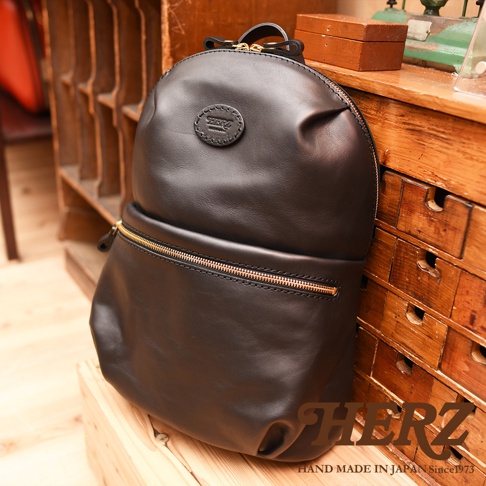 黑色職人手作皮革大開口圓角後背包，圓形壓印Logo，金色拉鍊，簡約設計。