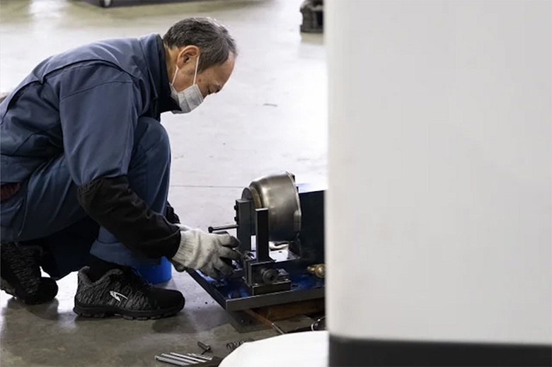 一位工人正在操作一台機器，機器上固定著一個不鏽鋼製的碗狀物體，碗狀物體表面光滑，呈現金屬光澤。