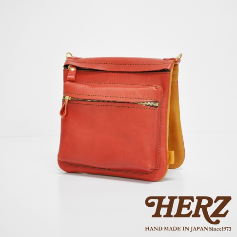 橘紅色皮革翻轉雙色直式斜背包，正面有拉鍊口袋，採用金屬拉鍊，皮革材質，純手工製作。