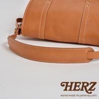 職人手作皮革復古郵差包，採用天然棕色皮革，以白色縫線點綴，展現精緻工藝。包包設計簡約，帶有可調節的寬版皮革背帶，適合日常攜帶。