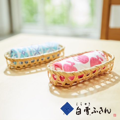 兩個竹籃裡各捲著一條友禪染白雪拭巾，一條印有藍色幾何圖案，另一條印有粉紅色兔子圖案。