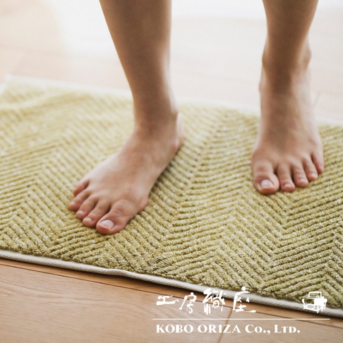 黃色人字紋快乾浴墊，質地為毛巾布，腳踩在浴墊上，浴墊邊緣為白色包邊。