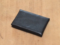 職人手作黑色皮革Organ雙開卡片收納夾，表面有細緻紋理，置於淺棕色木質背景上。