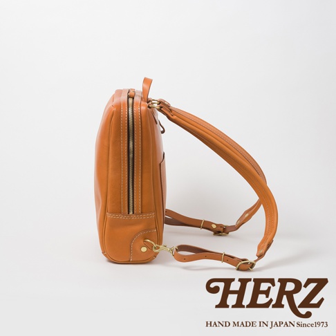 棕褐色皮革製成的商務後背包，側邊視角，展示拉鍊、縫線細節與皮質背帶，搭配金色金屬扣環。