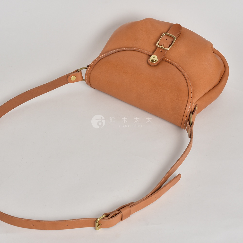 一個裝有金屬扣和肩帶的棕褐色皮革斜挎包，以白色背景展示。