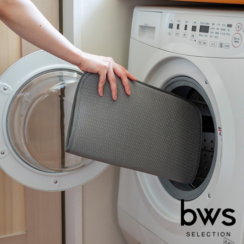 一只手正將灰色、表面有細小菱形紋路的折疊收納瀝水墊放入滾筒洗衣機的滾筒內。