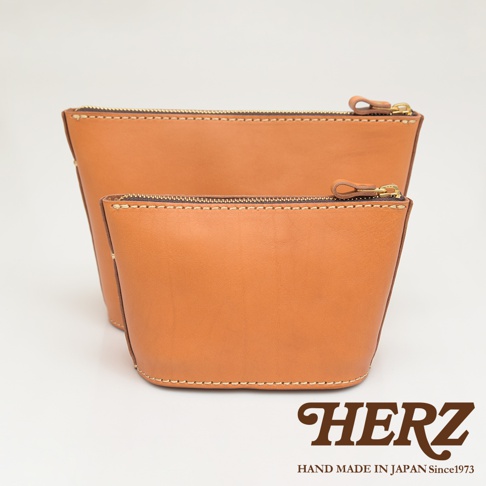 兩件棕色皮革三角收納包，大小不同，皆有拉鍊與皮質拉頭，手工縫線細緻，品牌標誌在右下角。