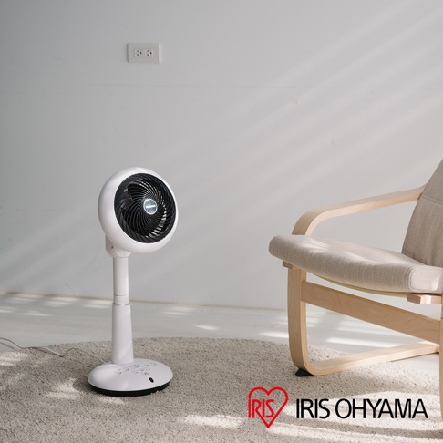 白色直立式循環扇，圓形扇頭，黑色扇網，可調式高度，放置於米色地毯上，旁邊有一張淺木色椅架、米色布面座椅的椅子。