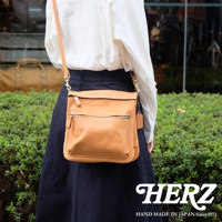 職人手作皮革翻轉雙色直式斜背包，採用淺棕色皮革製作，包身有兩層拉鍊口袋，搭配同色系縫線和金屬拉鍊。