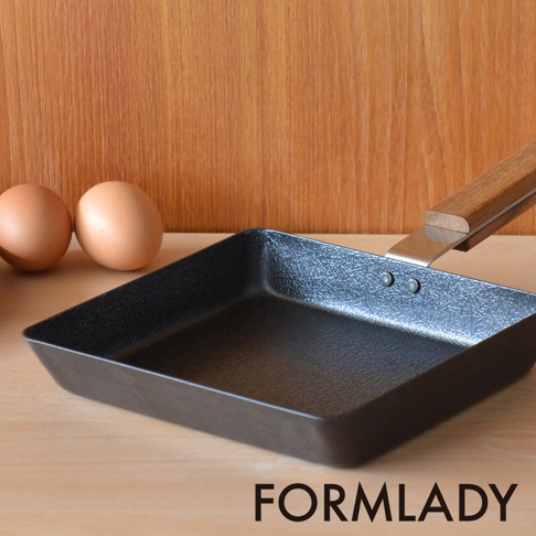 日製 ambai 玉子燒鐵鍋，L尺寸，鍋身黑色，表面有細緻紋理，搭配原木色木柄，鍋身側邊與木柄以金屬鉚釘固定，旁邊擺放兩顆雞蛋。