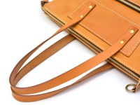 職人手作皮革威靈頓直式拉鍊托特包，呈現天然皮革溫潤的淺棕色調。包體結構清晰，帶有雙層皮革提把，以金屬鉚釘牢固固定。包身設有拉鍊開合，並點綴著精緻的縫線，展現細膩的工藝。